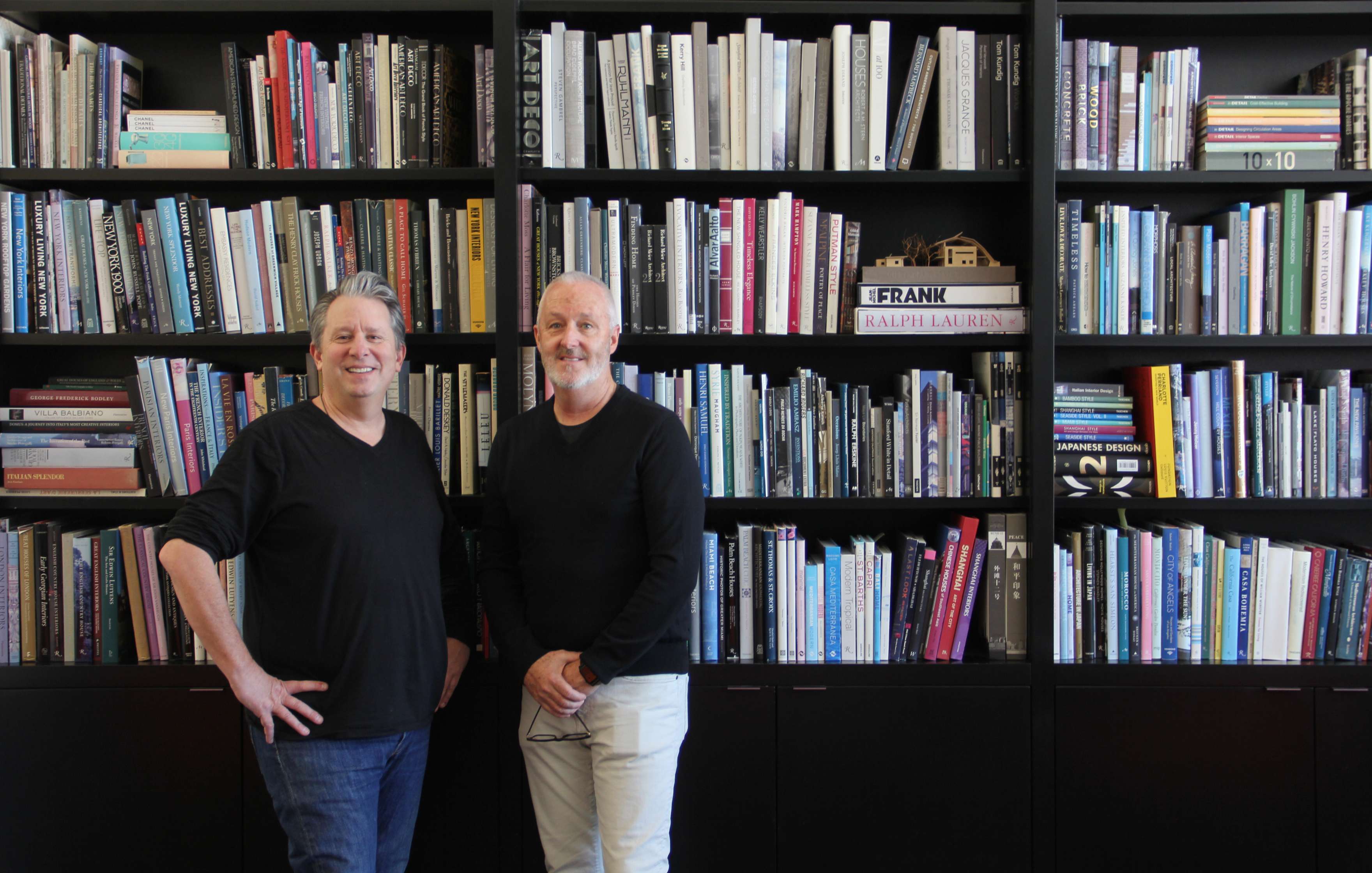 Michael Gilmore and Philip Weddle are standing in front of a tall bookshelf filled with a variety of books. Both men are smiling and dressed in casual attire.