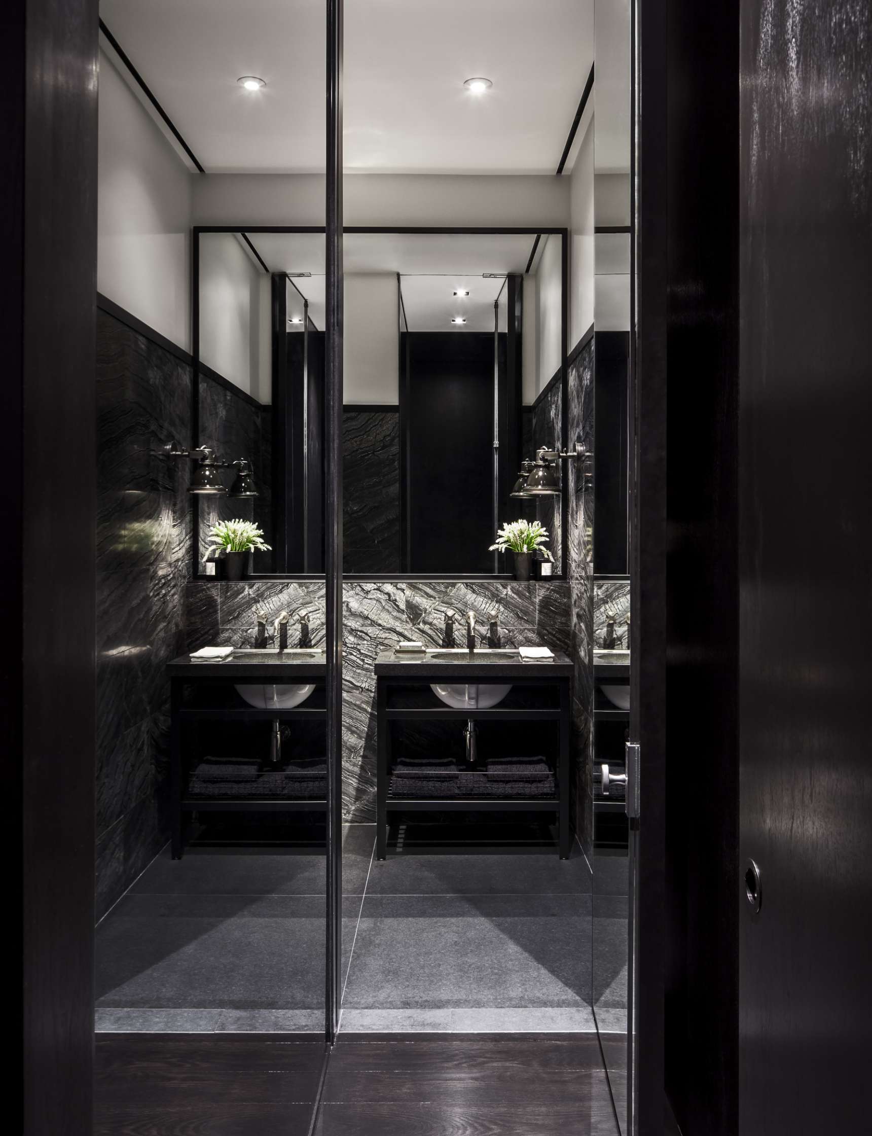 A modern bathroom features a double sink with a marble backsplash, black cabinetry, and mirrors on the walls, reflecting the contemporary design.