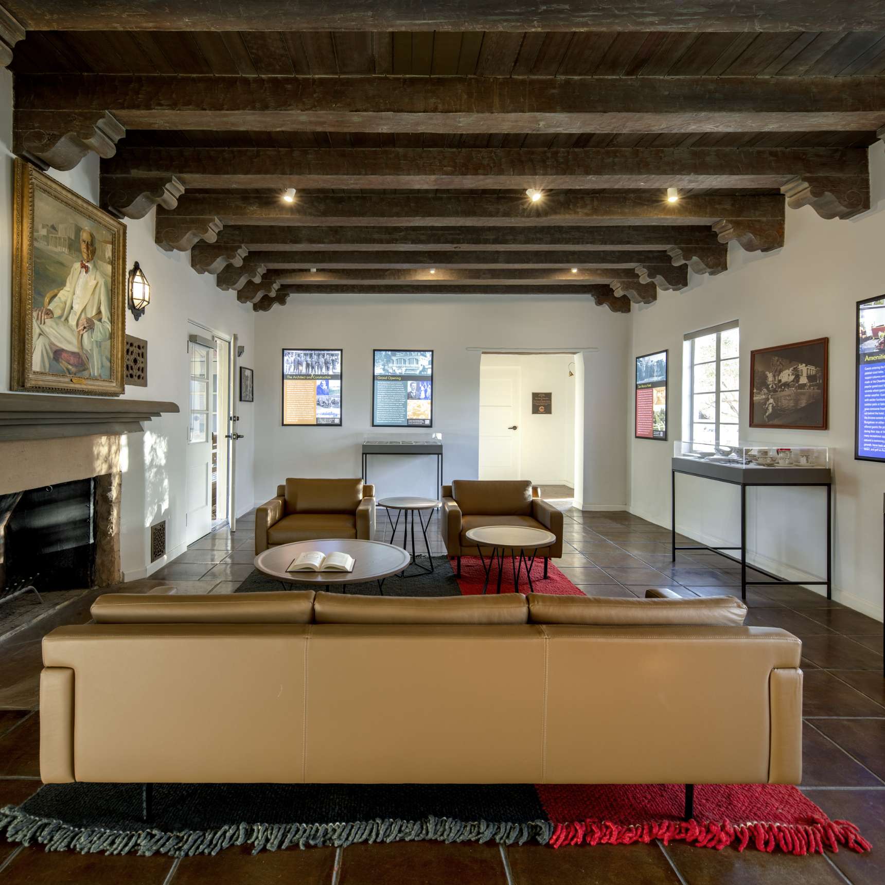 A modern living area with brown leather seating, a fireplace, and several framed artworks on the walls, decorated with red and blue rugs.