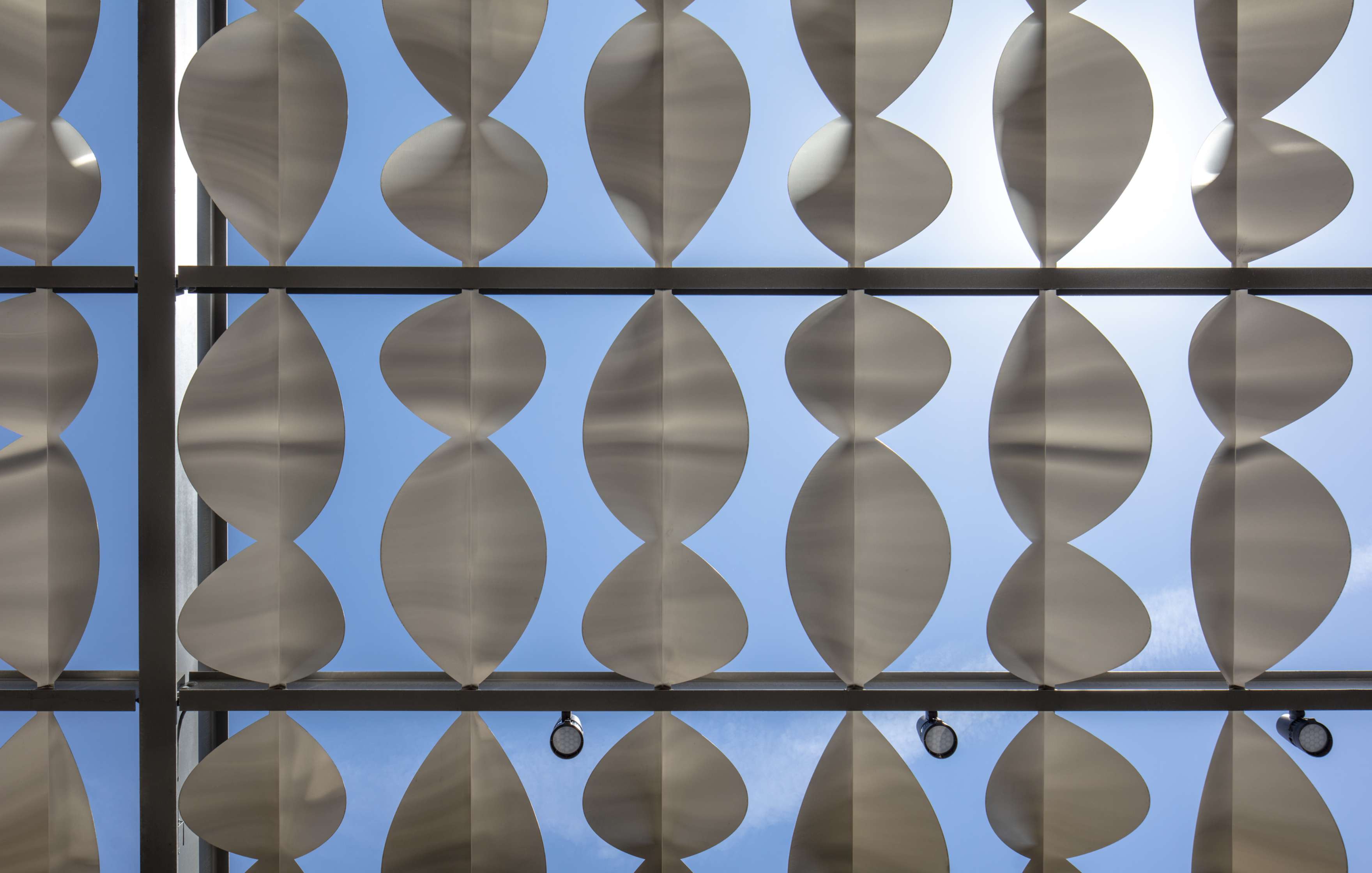 A ceiling structure composed of repeating, curved white panels against a backdrop of blue sky.