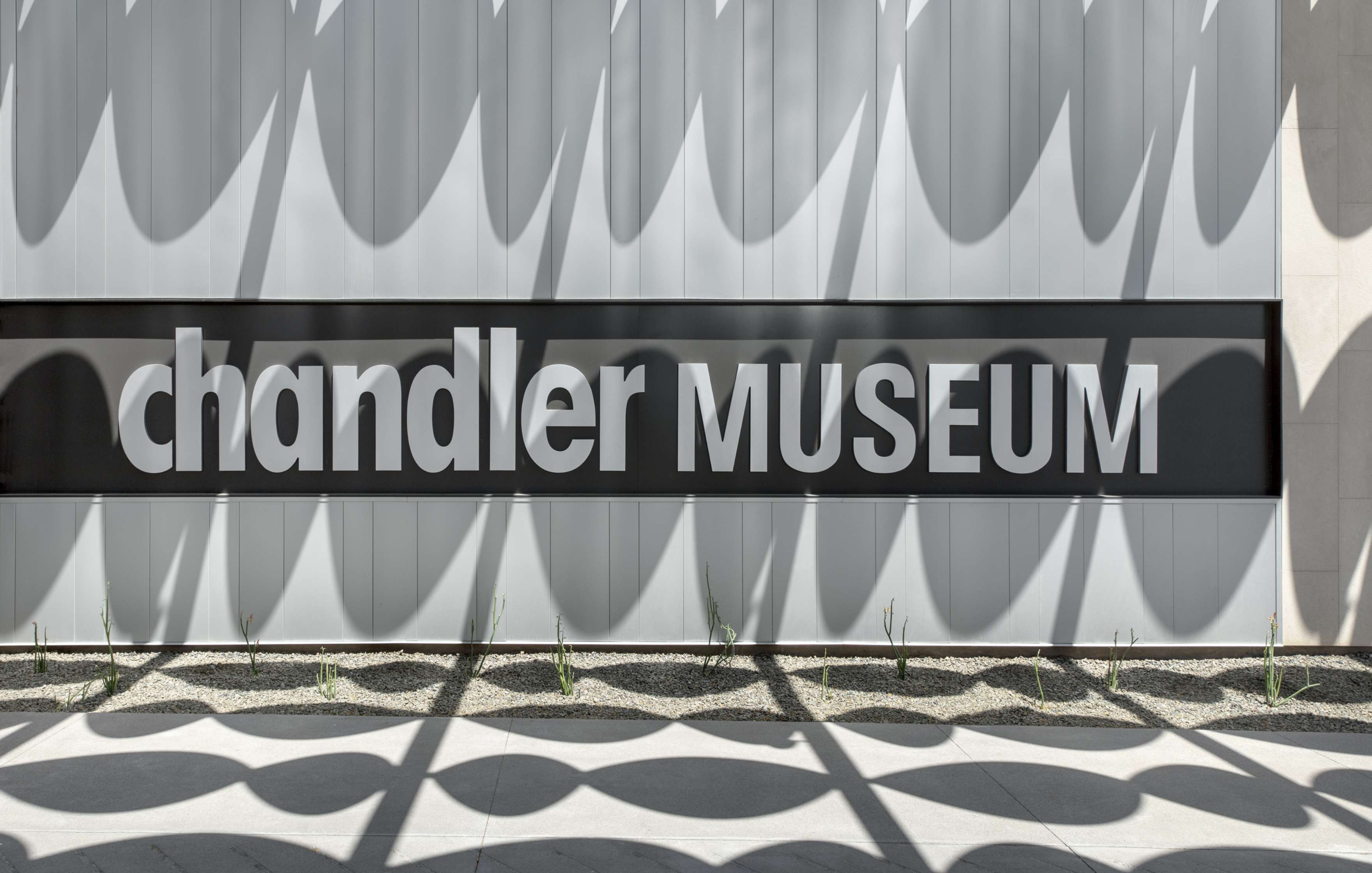 Sign reading “chandler MUSEUM” mounted on a building exterior with a patterned shadow overlay.