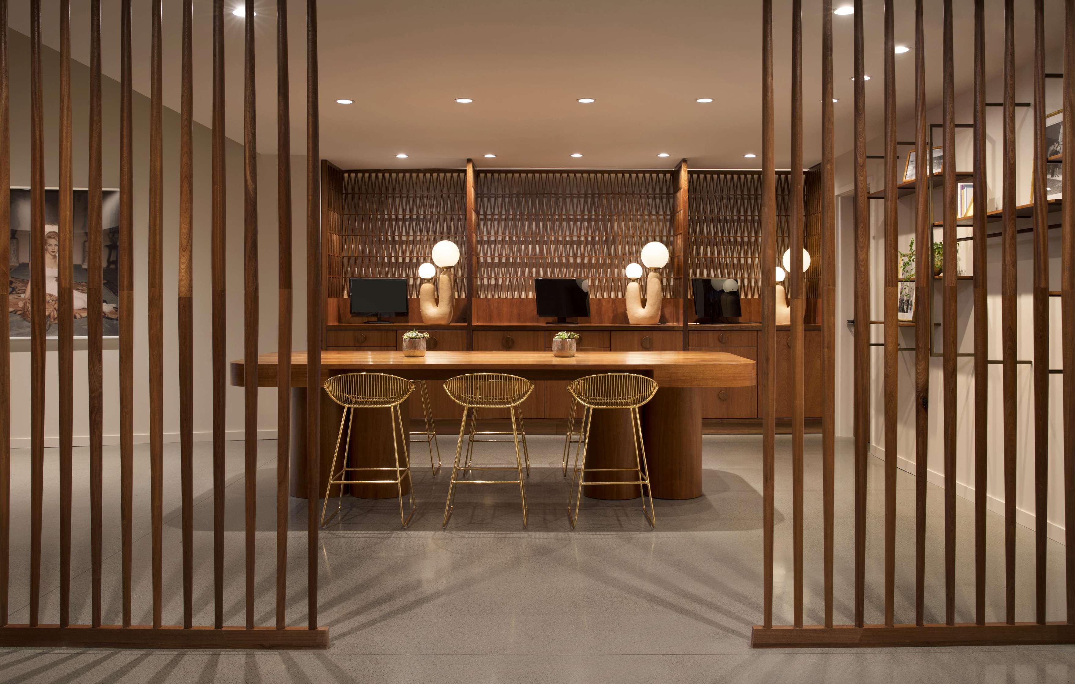 Modern, stylish office space featuring a wooden table with three chairs, partition screens, and multiple decorative light fixtures on the desk backdrop.