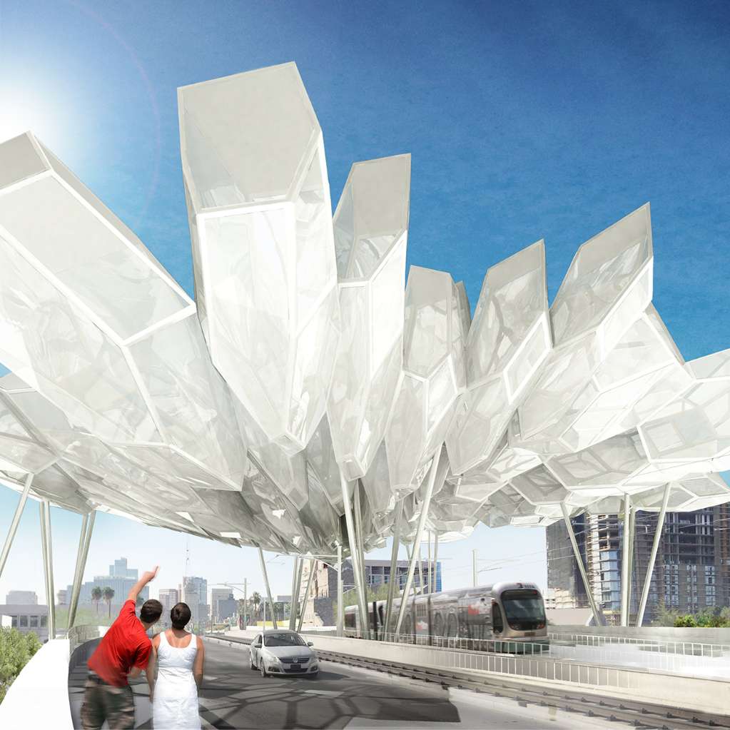 Two people stand on a bridge beneath a large, abstract modern canopy structure, with a car and a tram visible in the background against a clear blue sky.