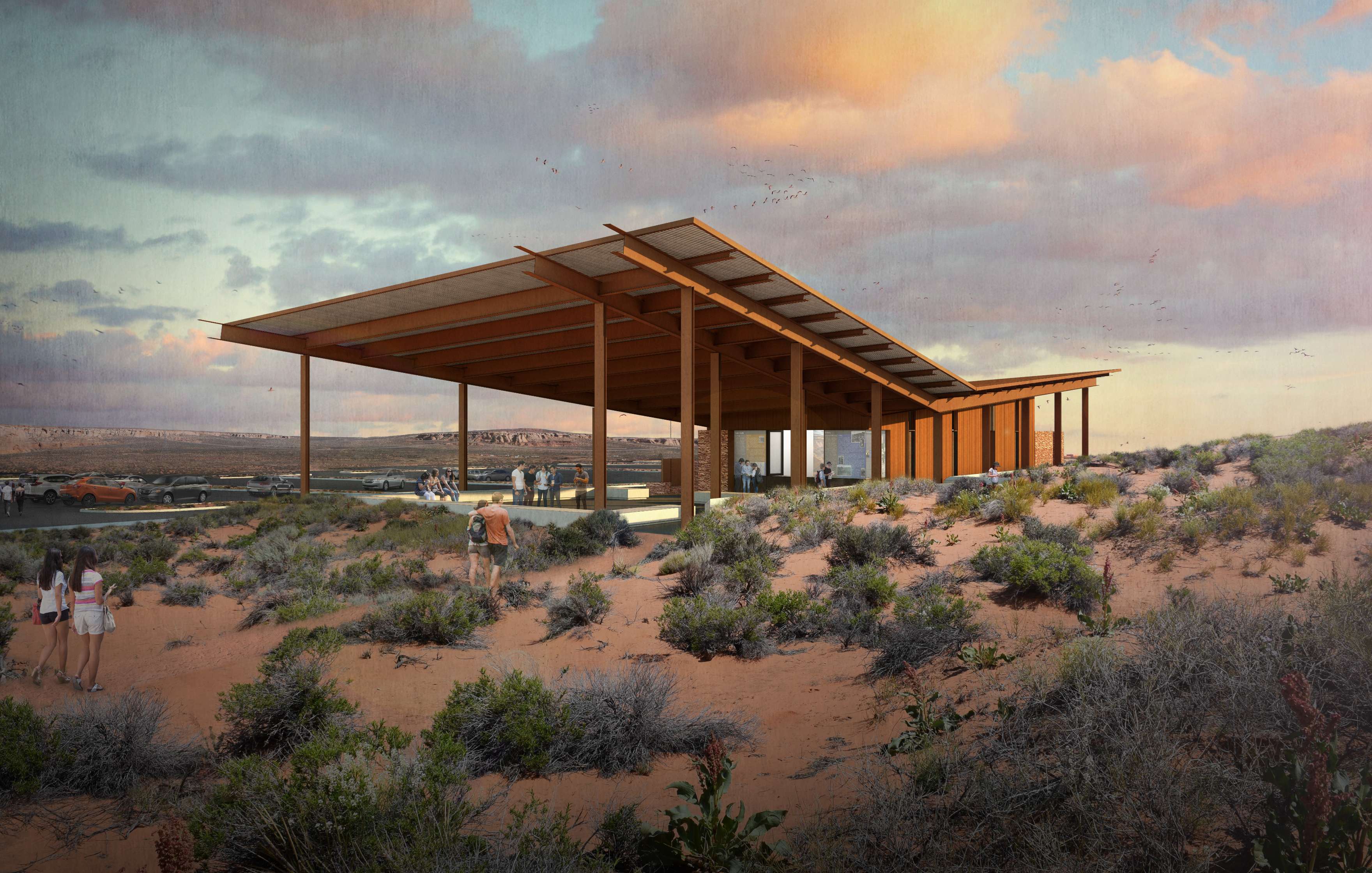 A modern building with a flat roof and wooden beams sits in a desert landscape with sparse vegetation. People are walking around the building. The sky is partly cloudy at sunset.