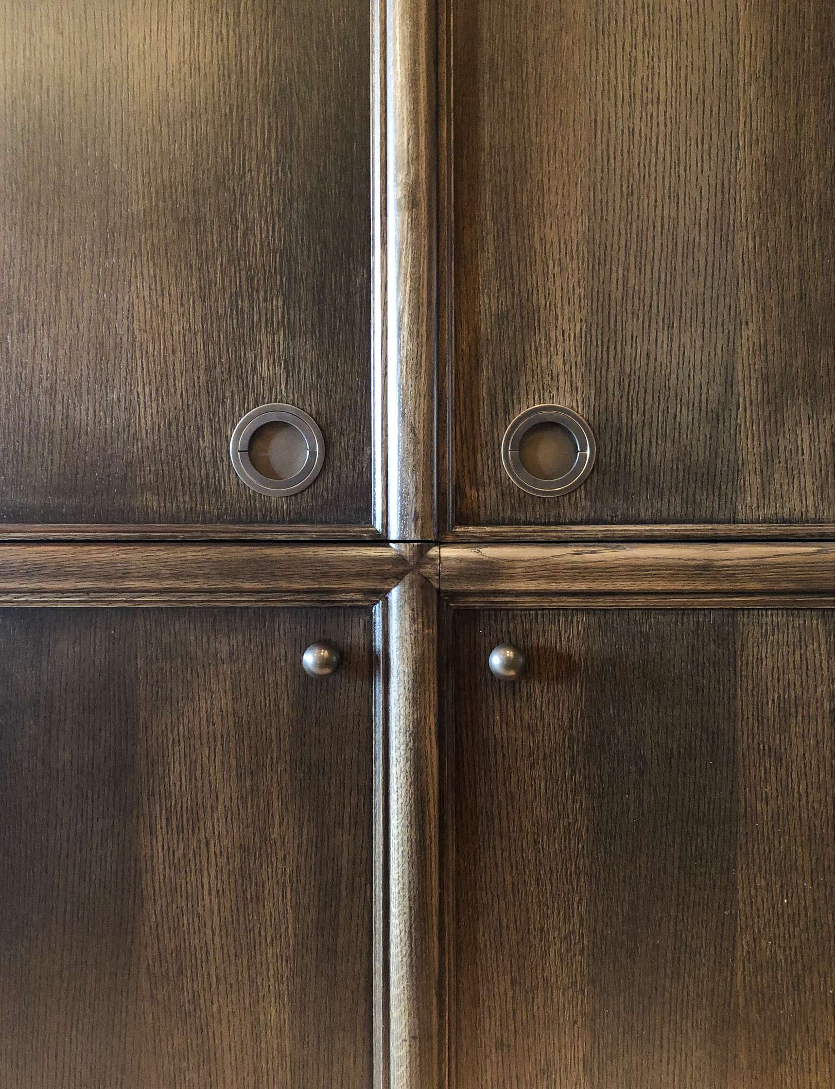 Close-up of a dark wood cabinet featuring round metal handles and circular inserts on the front doors.