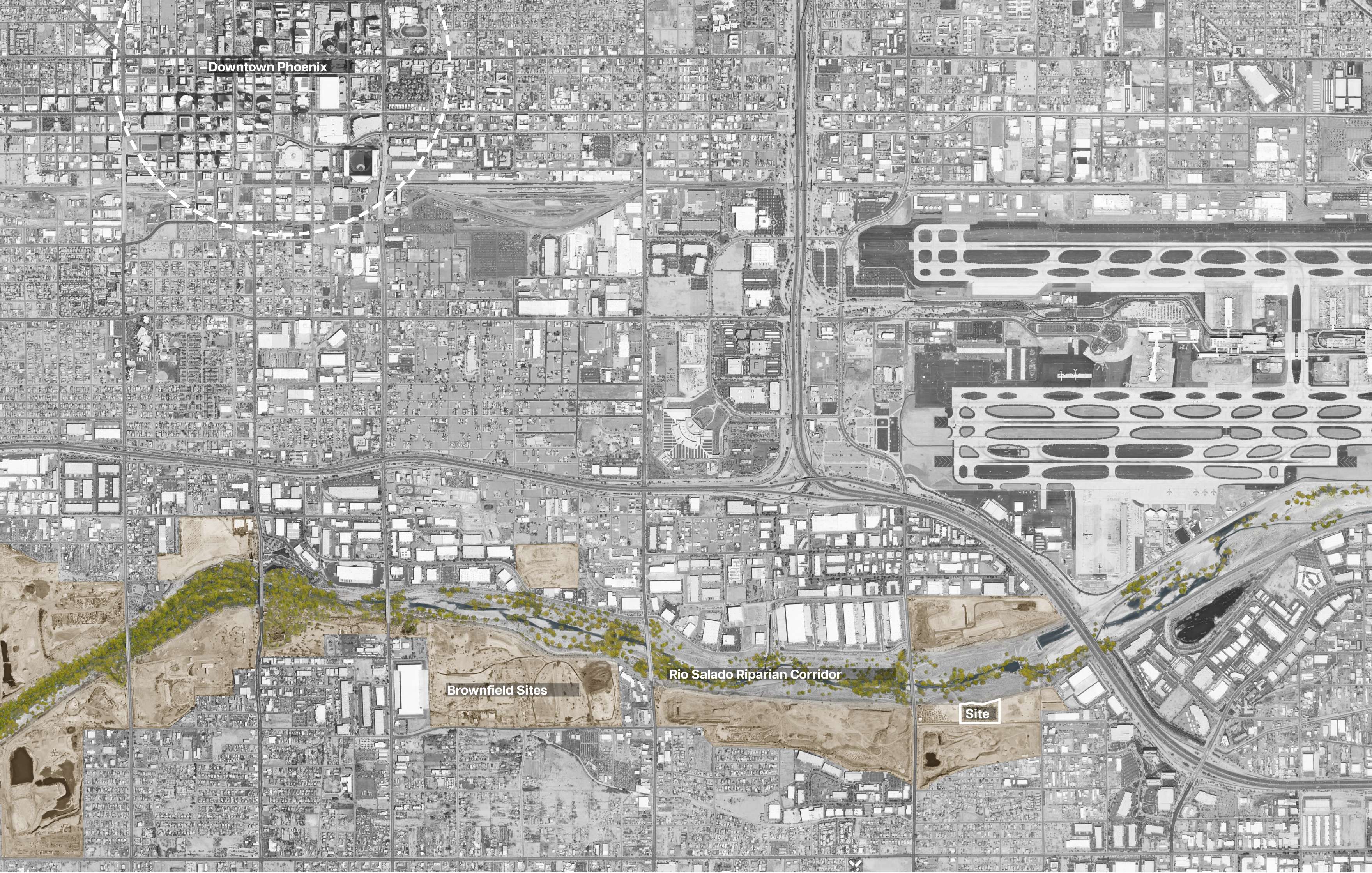 An aerial view of a desert landscape with a modern building complex surrounded by roads, parking lots, and scattered greenery, set against a backdrop of distant mountains.