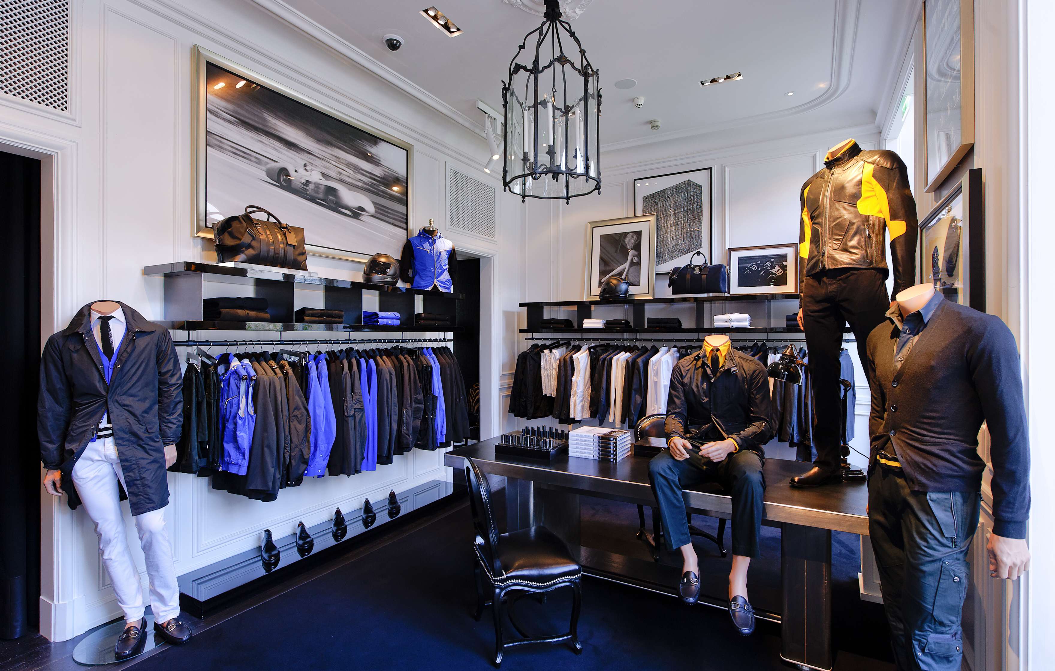 A high-end men's clothing boutique with neatly arranged shirts, jackets, pants, and accessories on racks and shelves, along with mannequins displaying outfits.