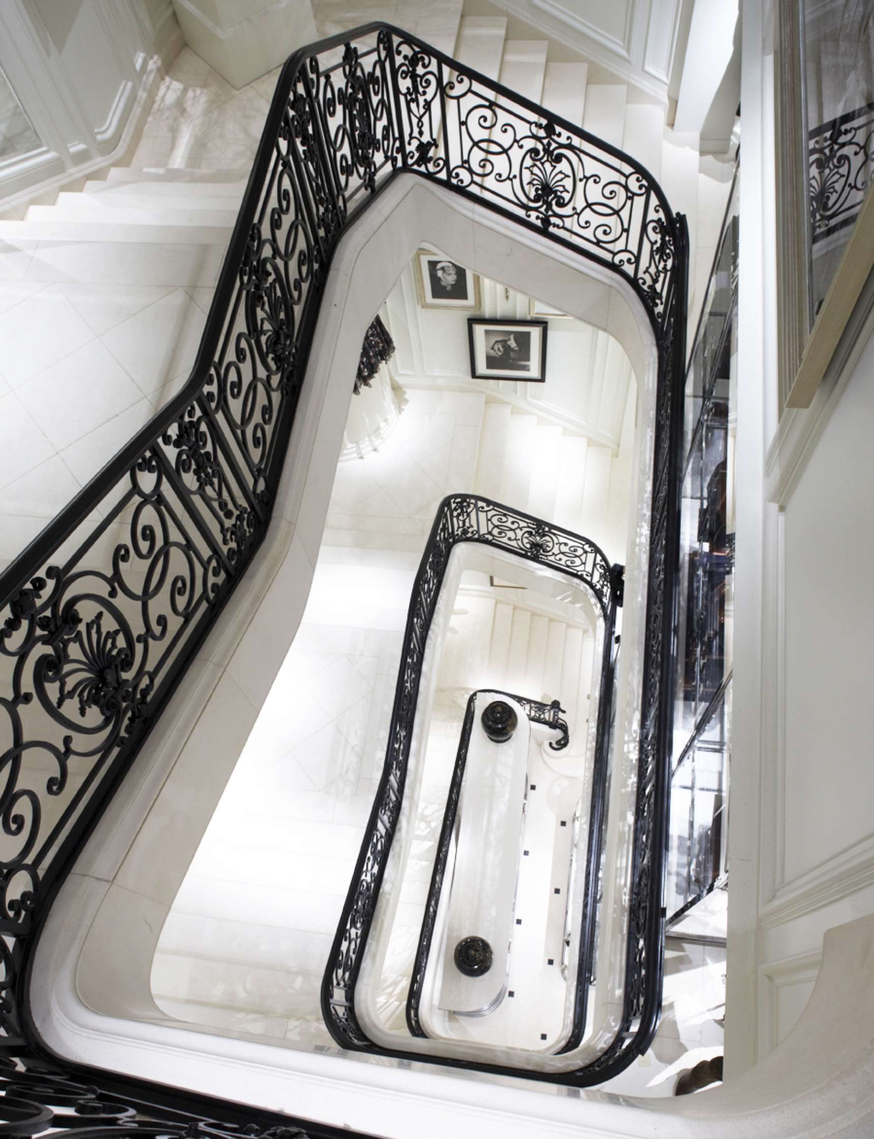 An overhead view of a multi-level stairwell with ornate black railings and white marble steps, decorated with framed black and white photos on the walls.