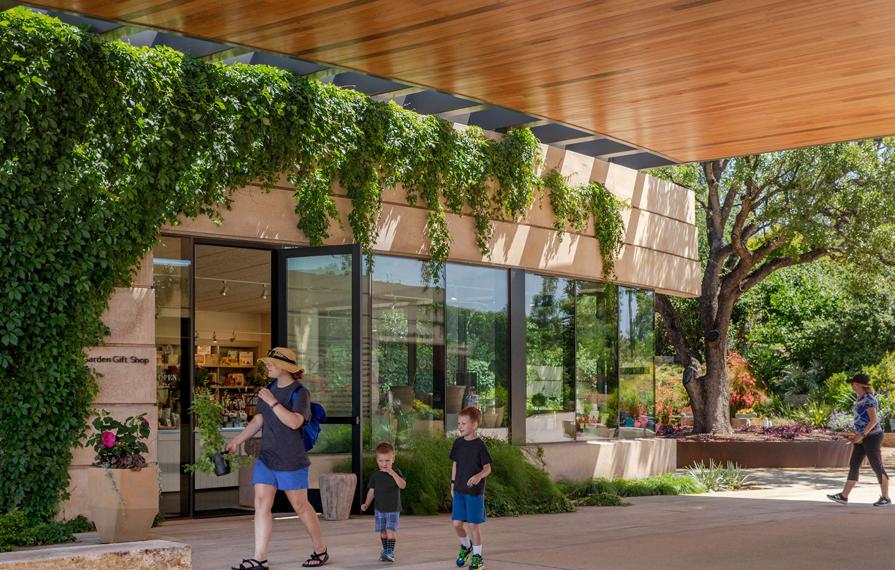 A woman and two children walk past a modern building with a green vine-covered facade and large windows.