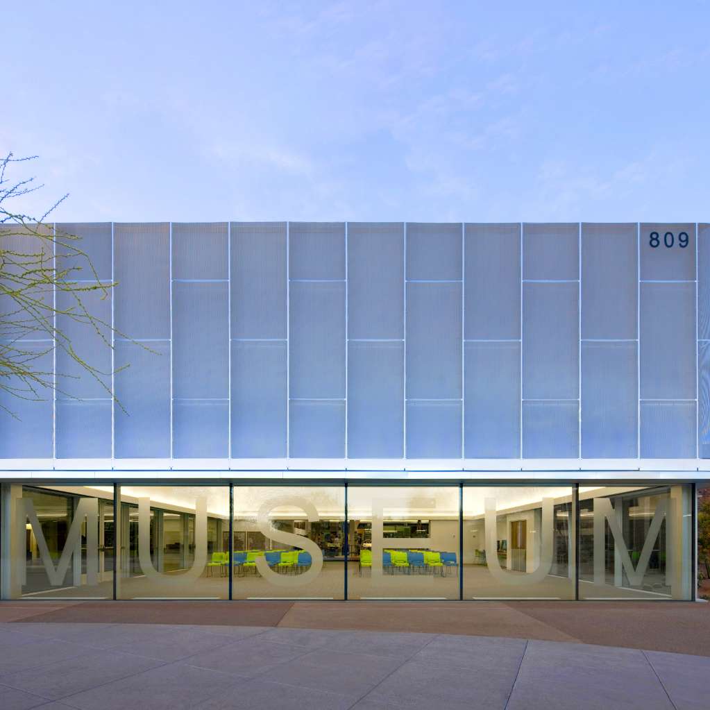 Modern building exterior featuring large glass windows with the word “MUSEUM” displayed. The address “809” is visible in the top corner.