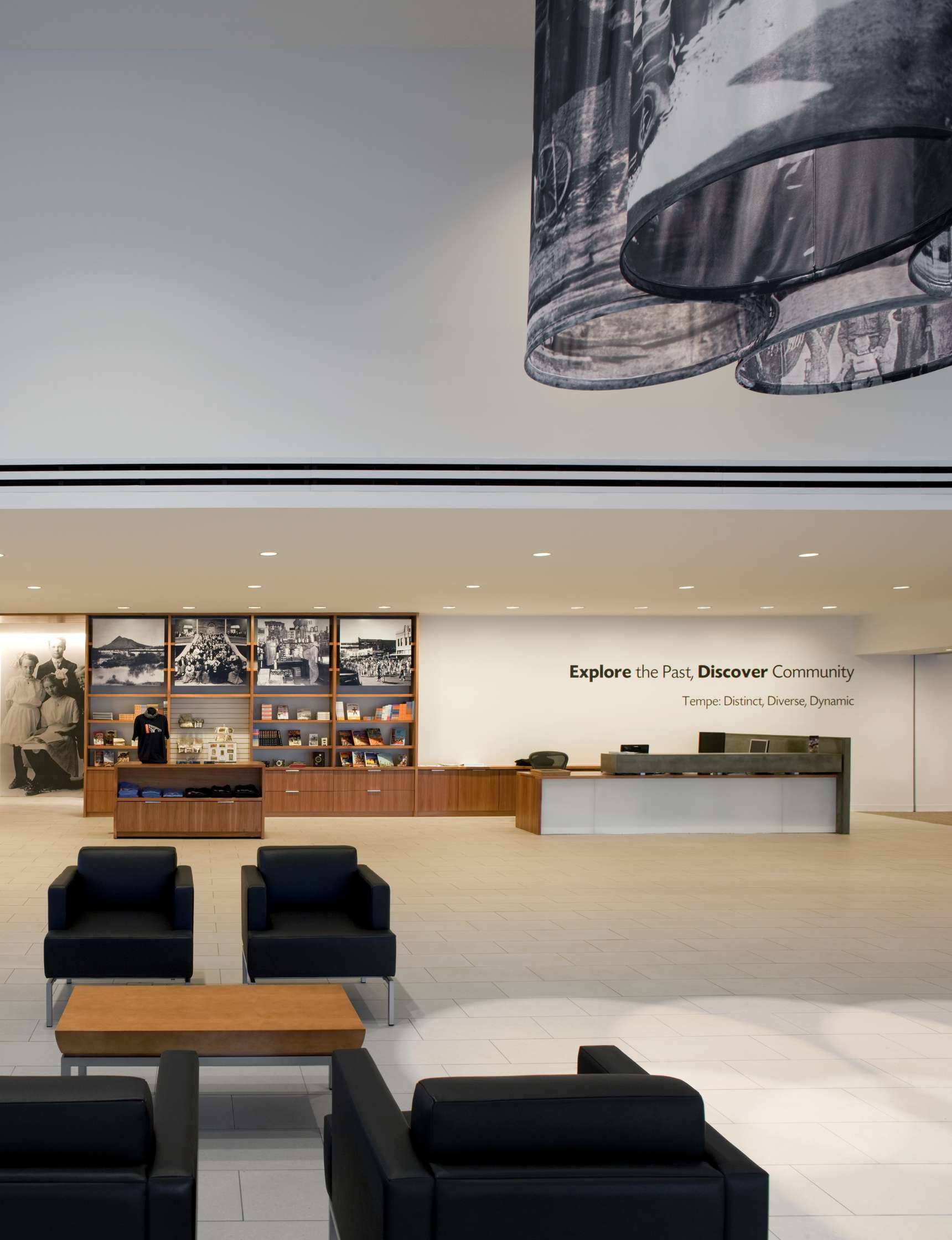 Museum lobby with informational displays on the back wall, a reception desk, and modern black seating in the foreground. A large hanging piece of art is visible in the upper part of the image.