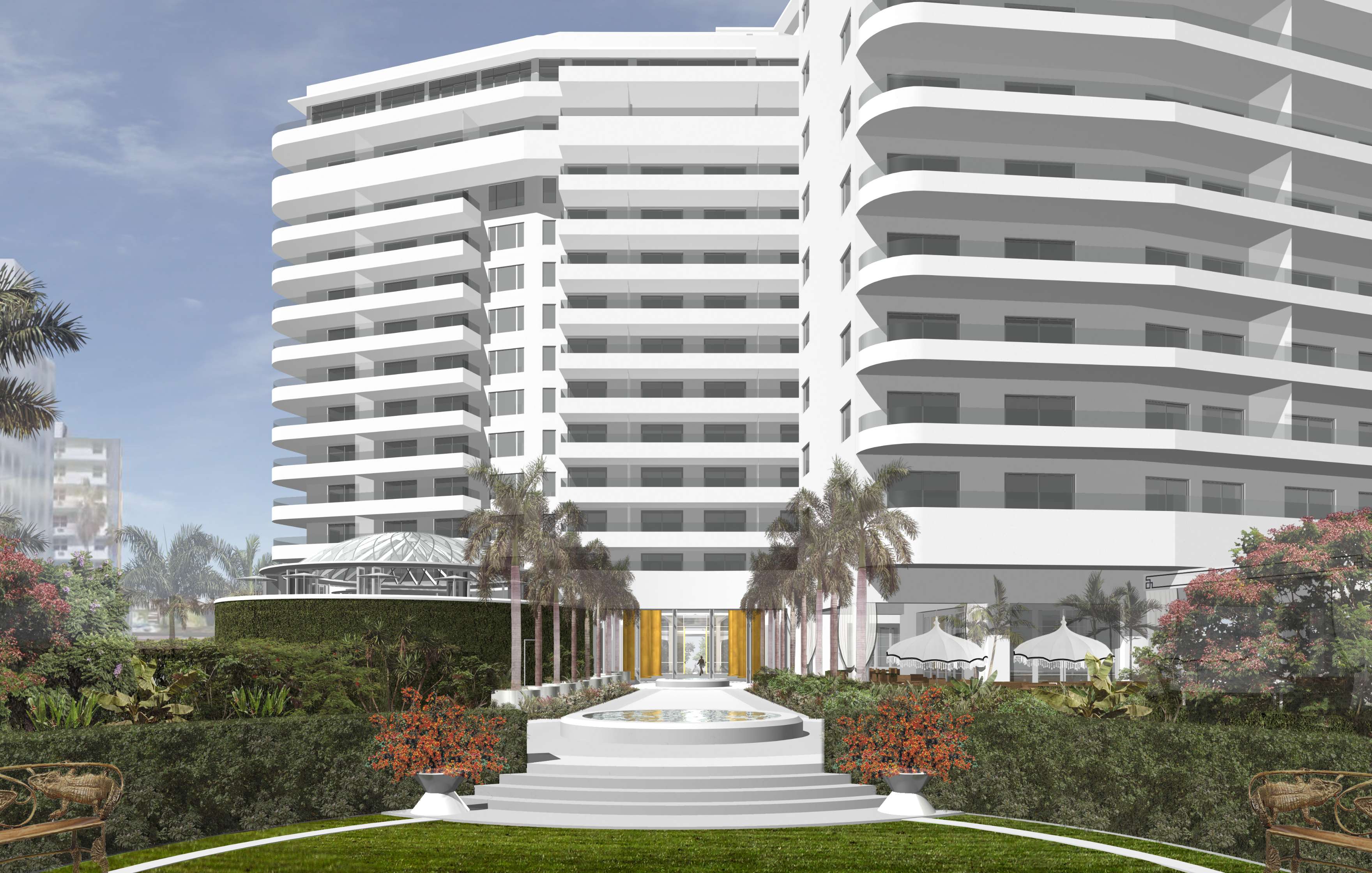 White modern building with multiple balconies, surrounded by landscaped gardens, palm trees, red flowers, and a central stone pathway leading to the entrance.