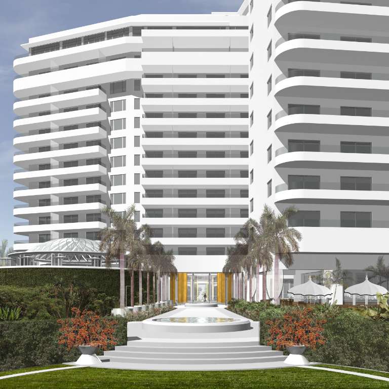 White modern building with multiple balconies, surrounded by landscaped gardens, palm trees, red flowers, and a central stone pathway leading to the entrance.