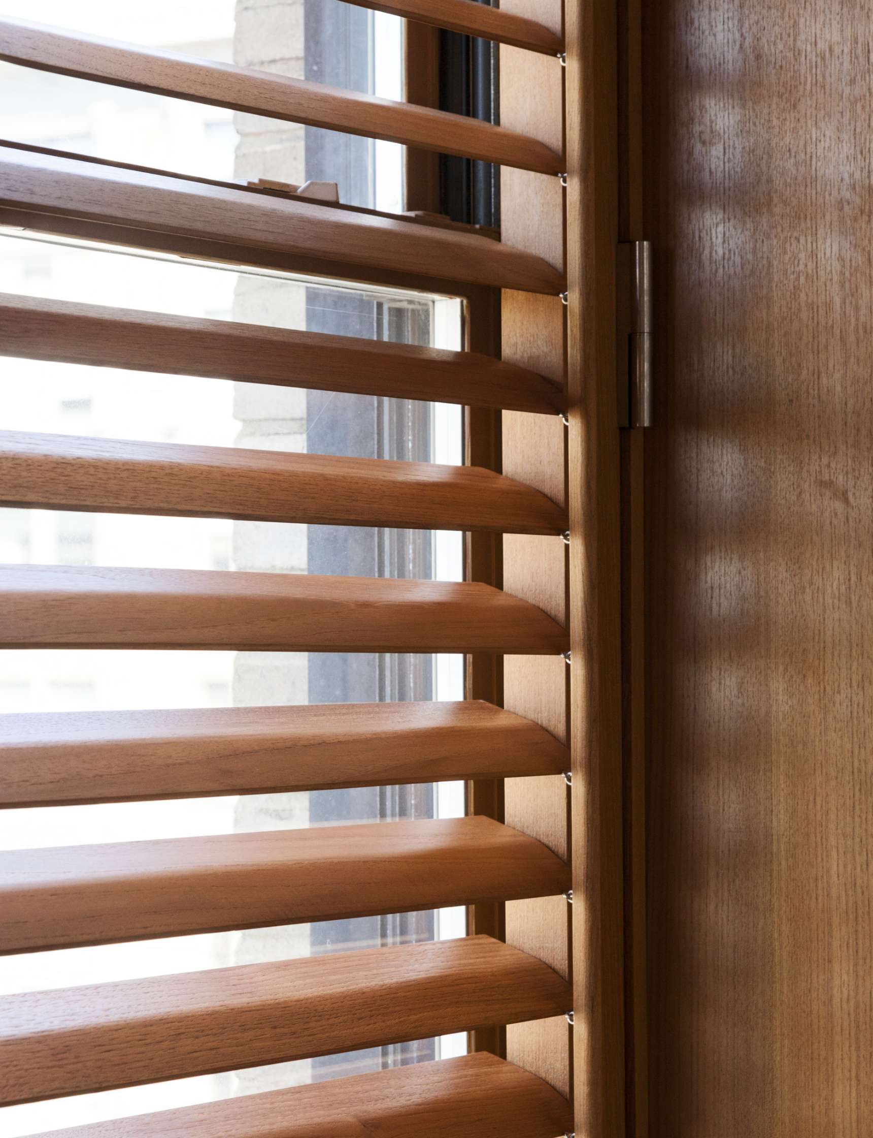 Close-up of wooden window blinds with horizontal slats partially open, allowing light to enter.