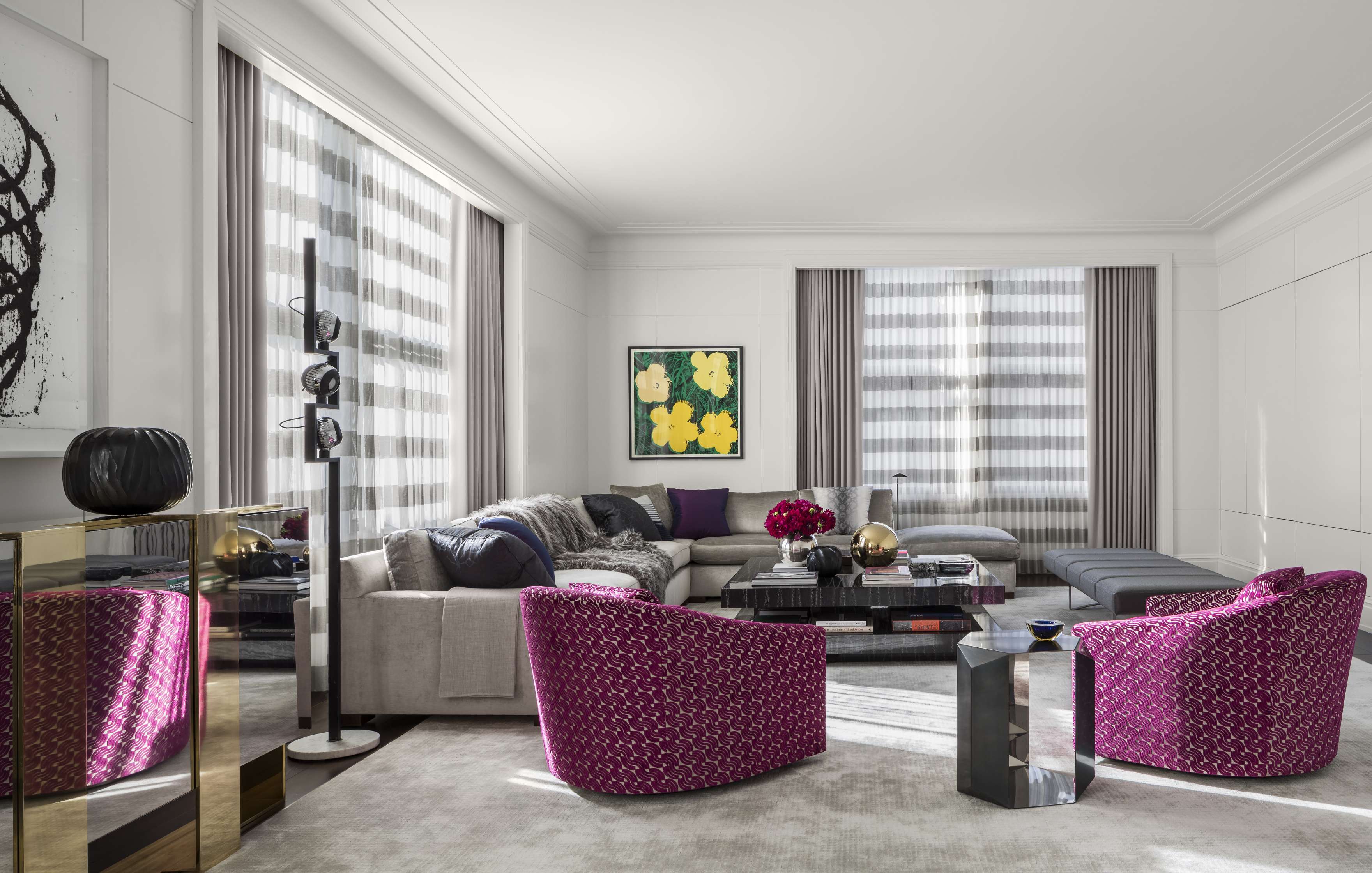 A modern living room with two purple armchairs, a large L-shaped sofa, coffee table, window drapes, wall art, and decor items.