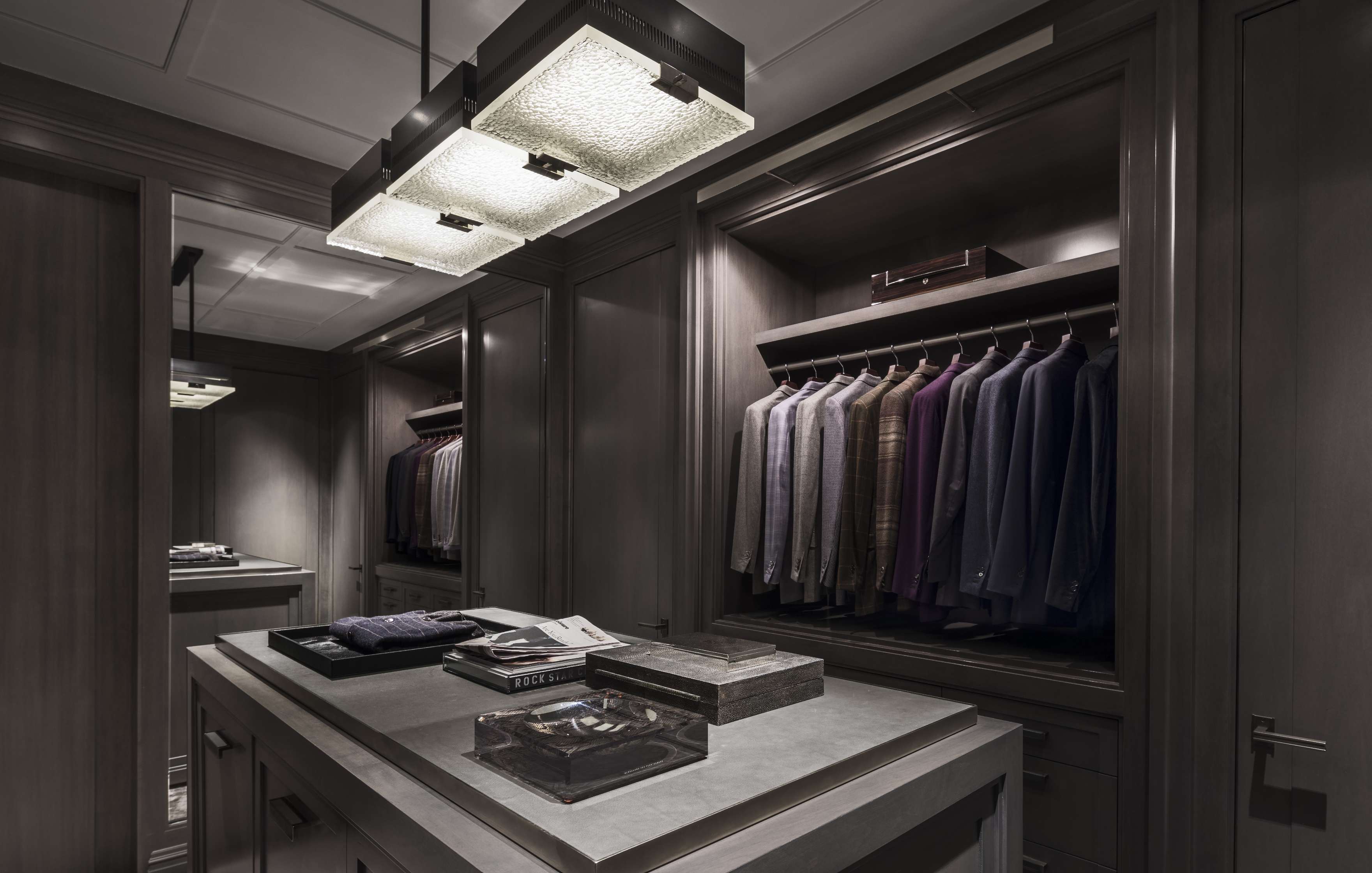 A walk-in closet with suits hanging on a rack, shelves with various items, and overhead lighting.