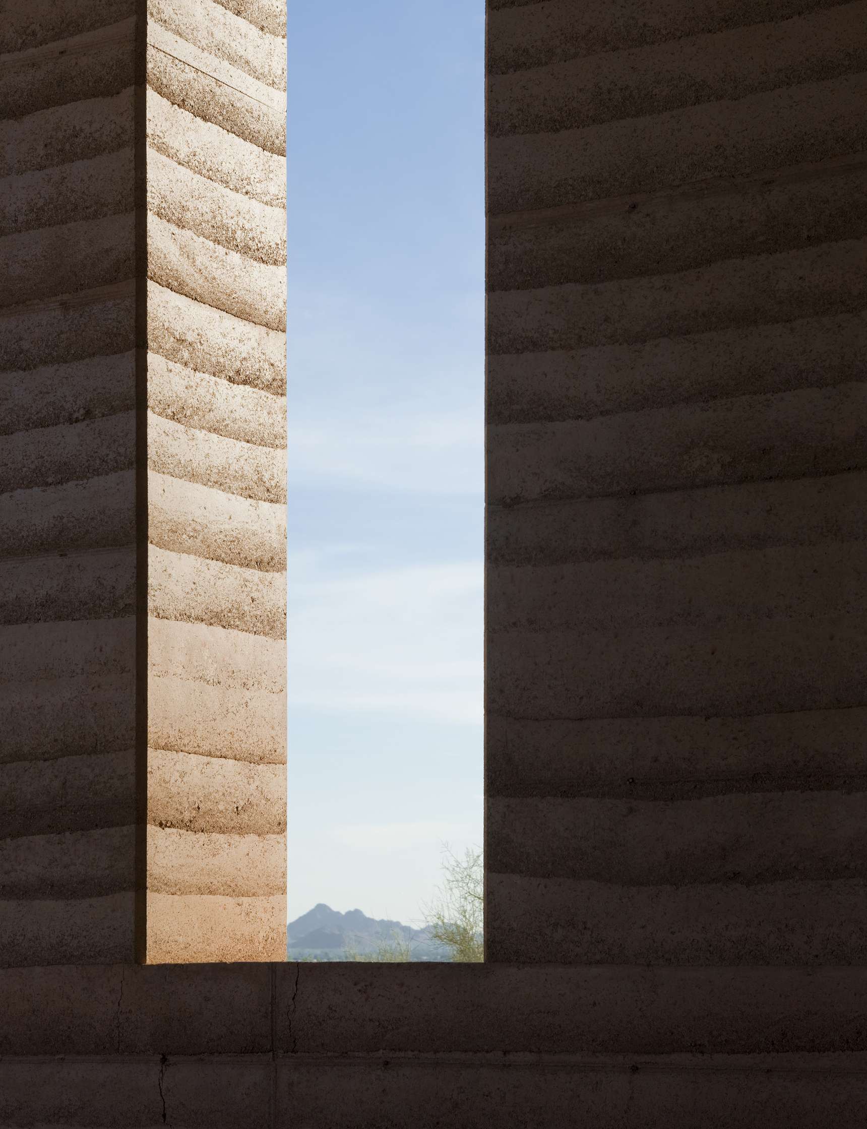 Two textured, vertically aligned walls with a narrow gap between them revealing a distant view of hills and a partly cloudy sky.