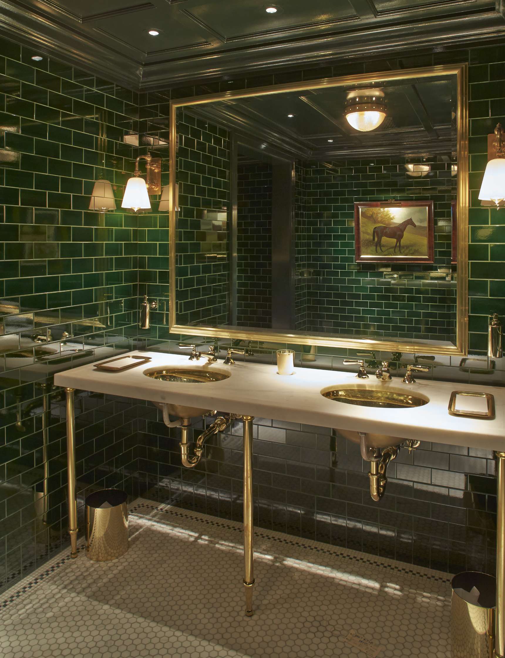 A luxurious bathroom with brass fixtures, two sinks, a large mirror, green tile walls, and a painting of a horse.