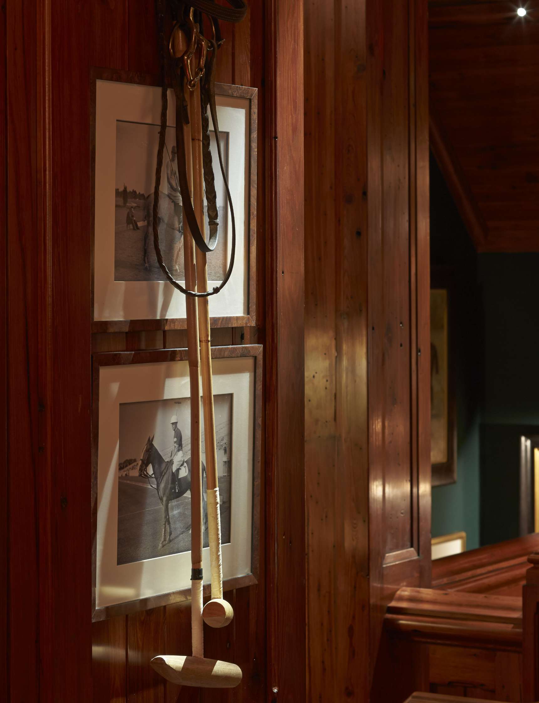 Wooden polo mallets hang on a wooden wall next to framed black-and-white photographs of polo players.